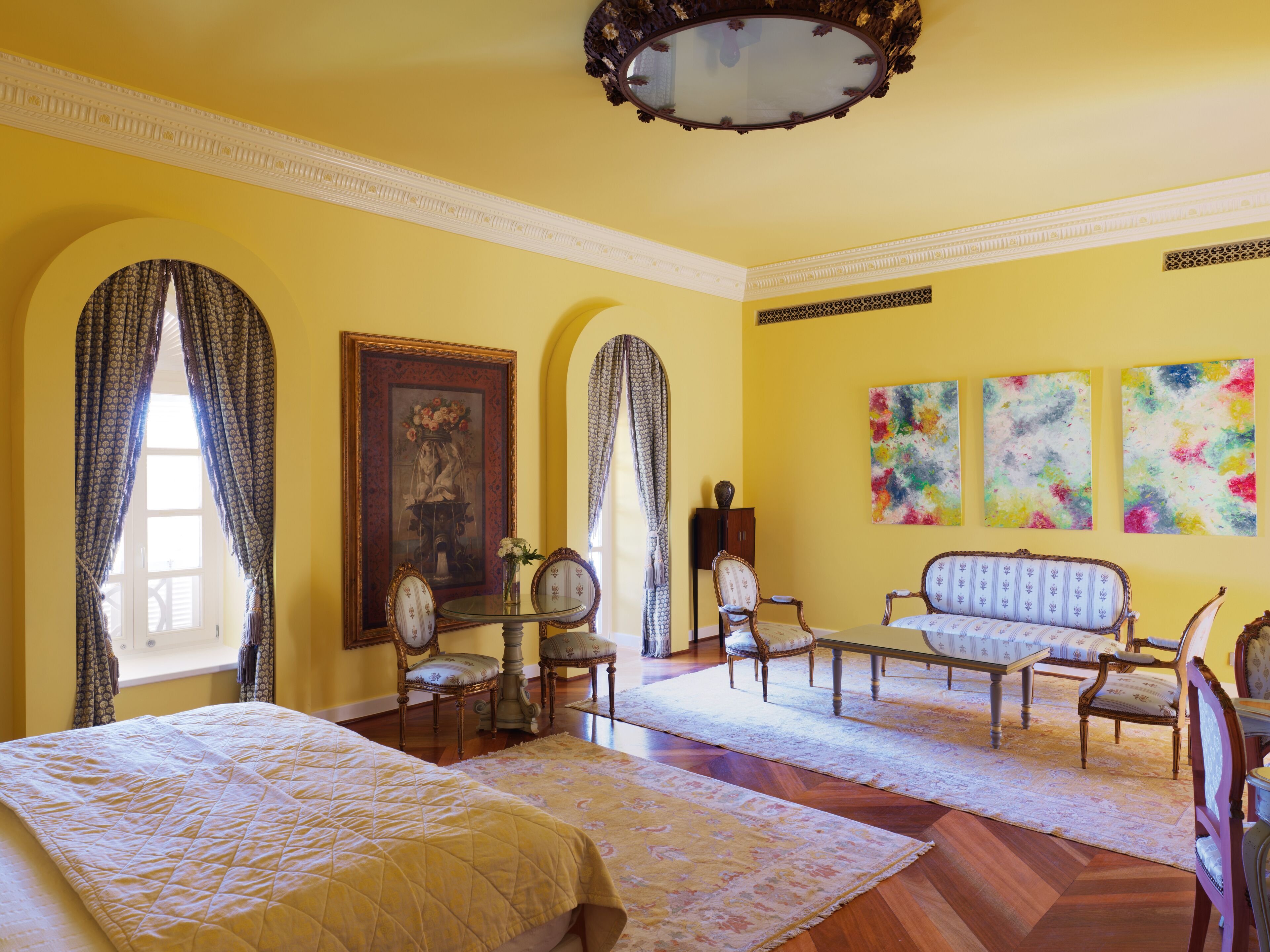 A room with a large bed, two armchairs, a sofa, a table with a vase, and a painting on the wall.