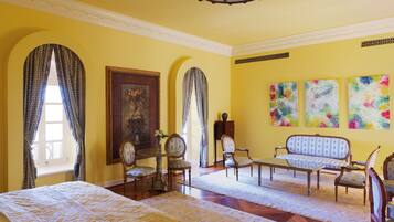A room with a large bed, two armchairs, a sofa, a table with a vase, and a painting on the wall.