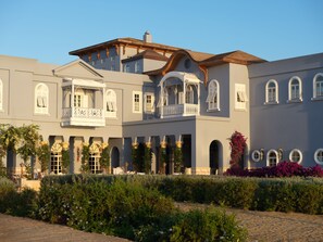 A multi-story building with a balcony, arched windows, and a garden area with various plants. - La Maison Bleue (El Gouna)