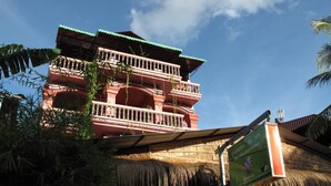 Un edificio de varios pisos con un estilo arquitectónico tradicional, que presenta balcones y una estructura de techo de paja.