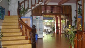 Un vestíbulo de hotel con una escalera de madera, un mostrador de recepción y un vidrio que da al área de comedor.