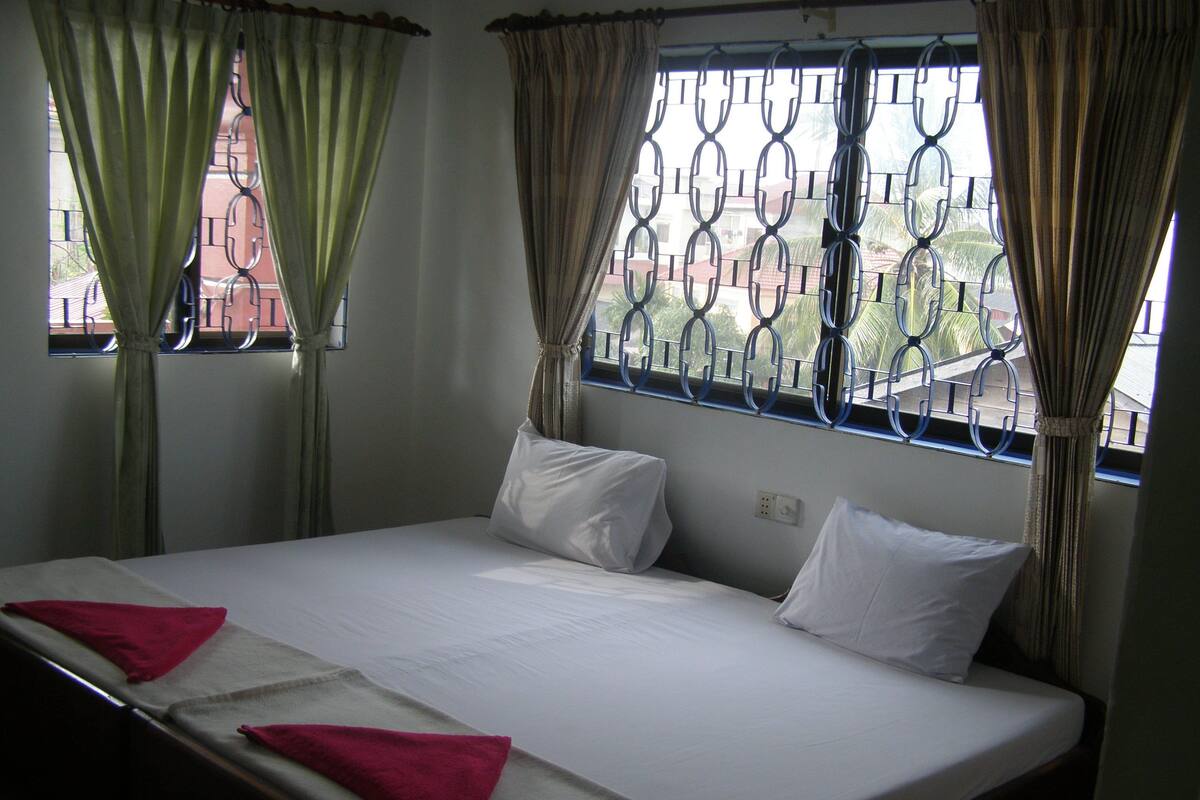 A single-bed room with a window featuring metal bars and curtains.