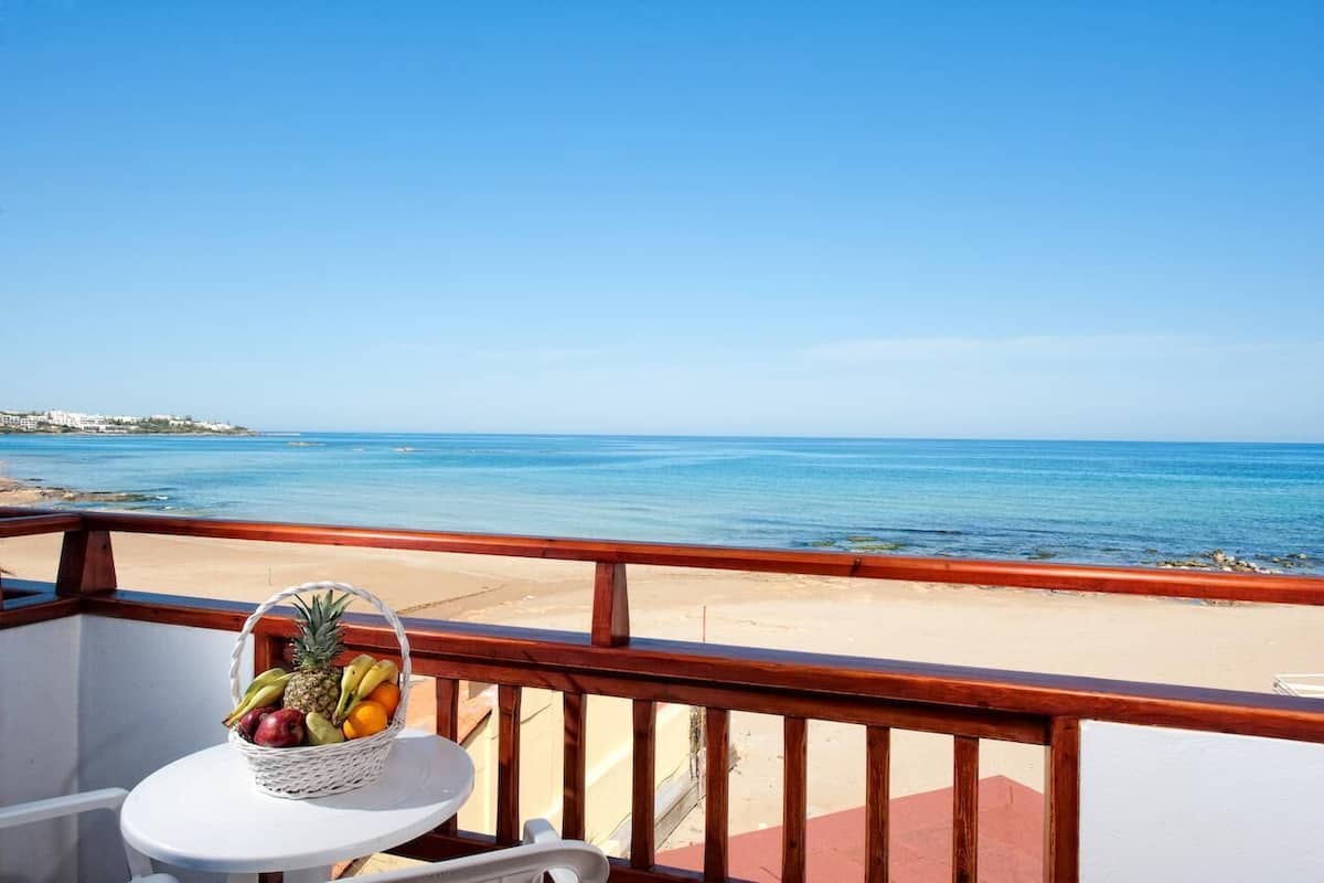 A balcony with a wicker basket of fruit, a white chair, and a view of the beach and ocean.