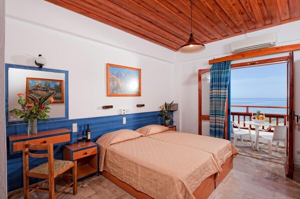 A bedroom with a bed, a desk, and a chair. There is a window with a view of the sea. - Vlachakis Hotel (Hersonissos)