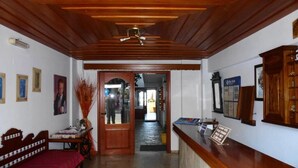 A reception area with a wooden reception desk, a sofa, and a bed. There is a door leading to another room. - Vlachakis Hotel (Hersonissos)