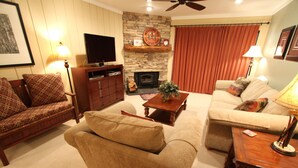 Una sala de estar con chimenea, sofás, televisor y ventilador de techo.