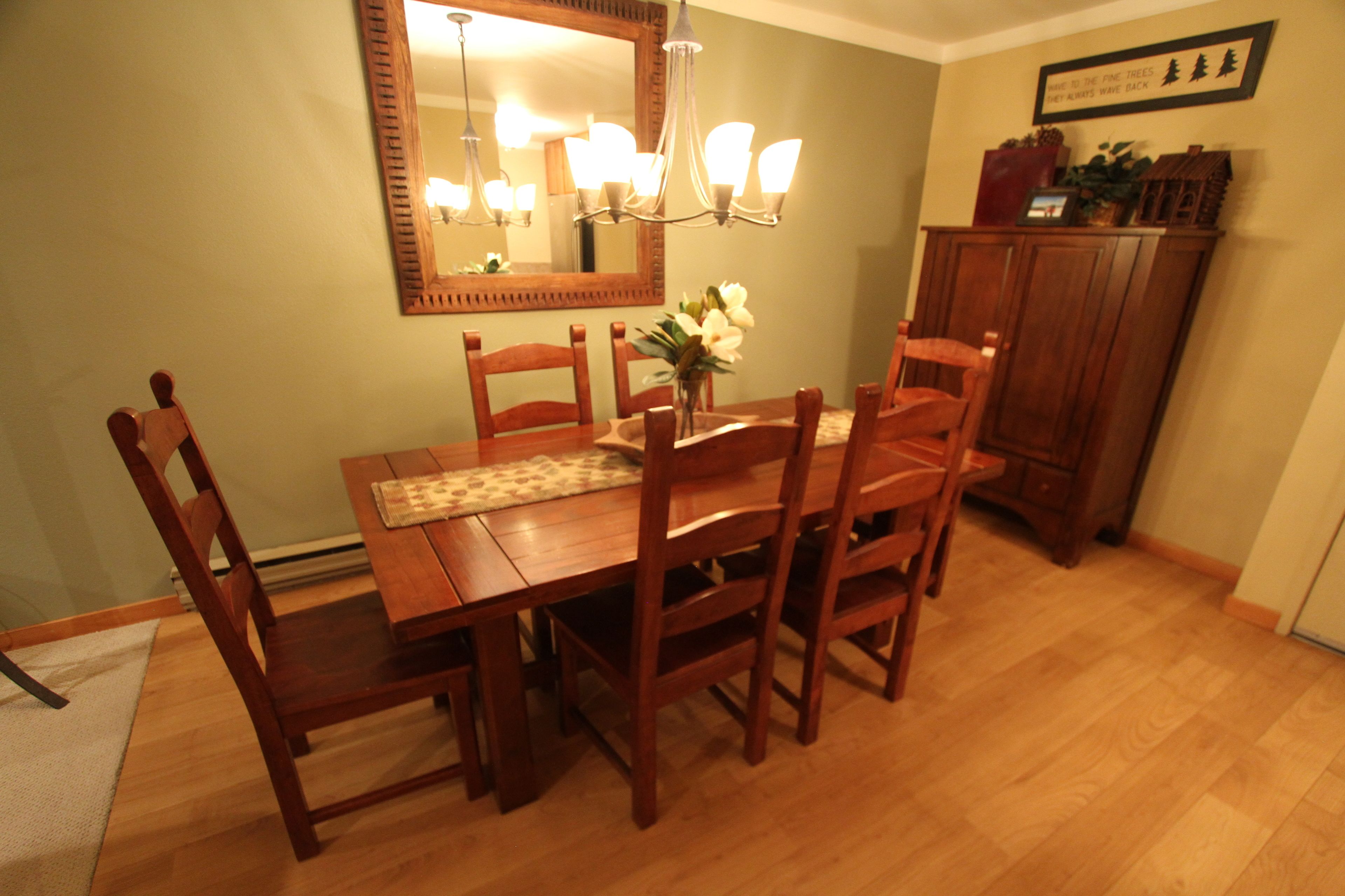 A dining room with a wooden table and chairs, a chandelier, and a mirror on the wall.