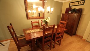 Un comedor con una mesa y sillas de madera, una araña y un espejo en la pared.