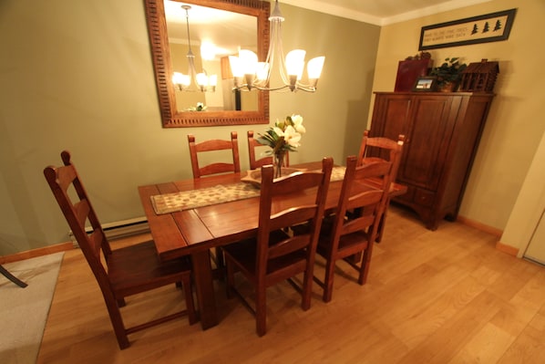 Un comedor con una mesa y sillas de madera, una araña y un espejo en la pared.