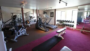 Un gimnasio con equipo de ejercicio, cinta de correr, mancuernas y banco.