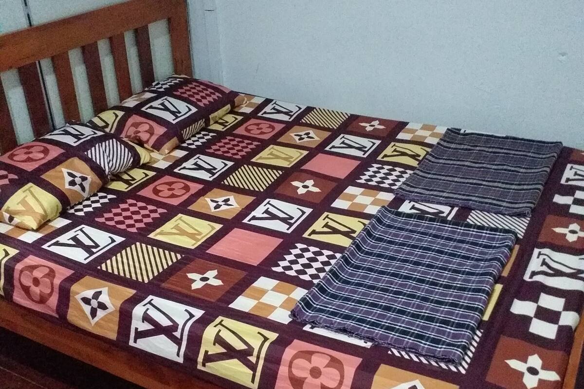 Una cama individual con una colcha estampada y almohadas, un cabecero de madera y una pared lisa de fondo.