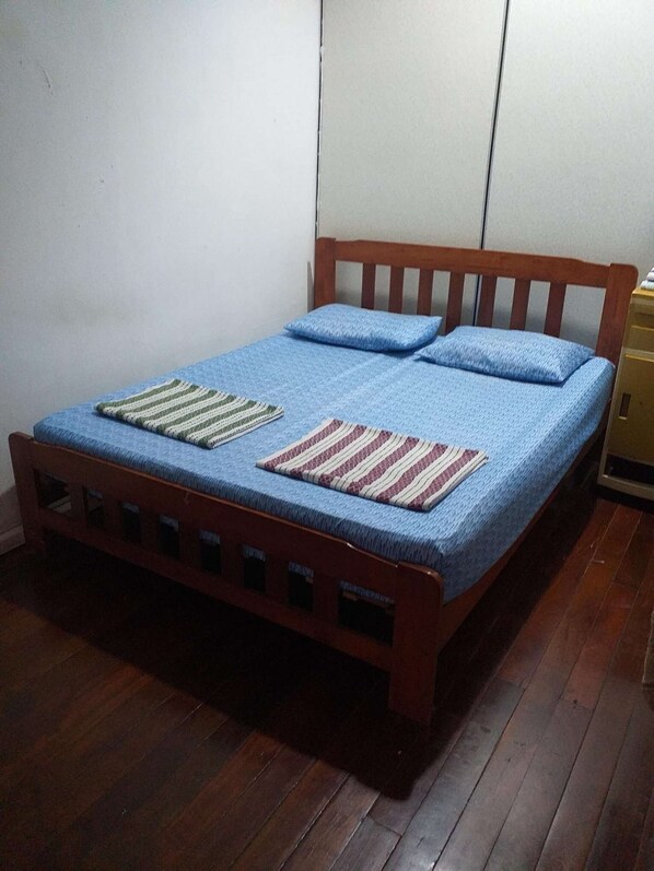 A single bed with a wooden frame and blue bedding, a small bedside table, and a striped rug on the floor.