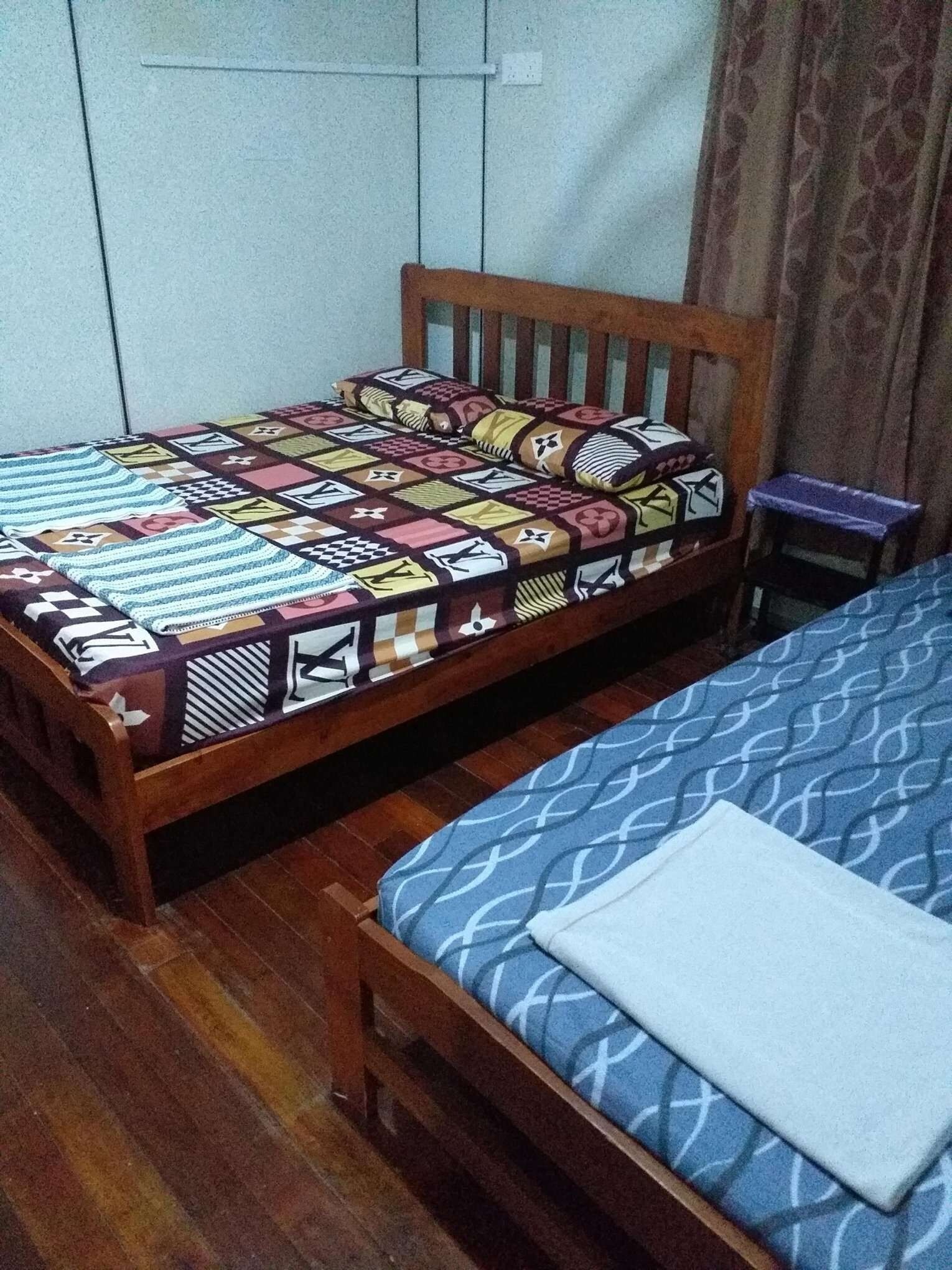 Ein kleines Zimmer mit einem Einzelbett, einem hölzernen Bettgestell, einer gemusterten Tagesdecke und einer blauen Matratzenauflage.