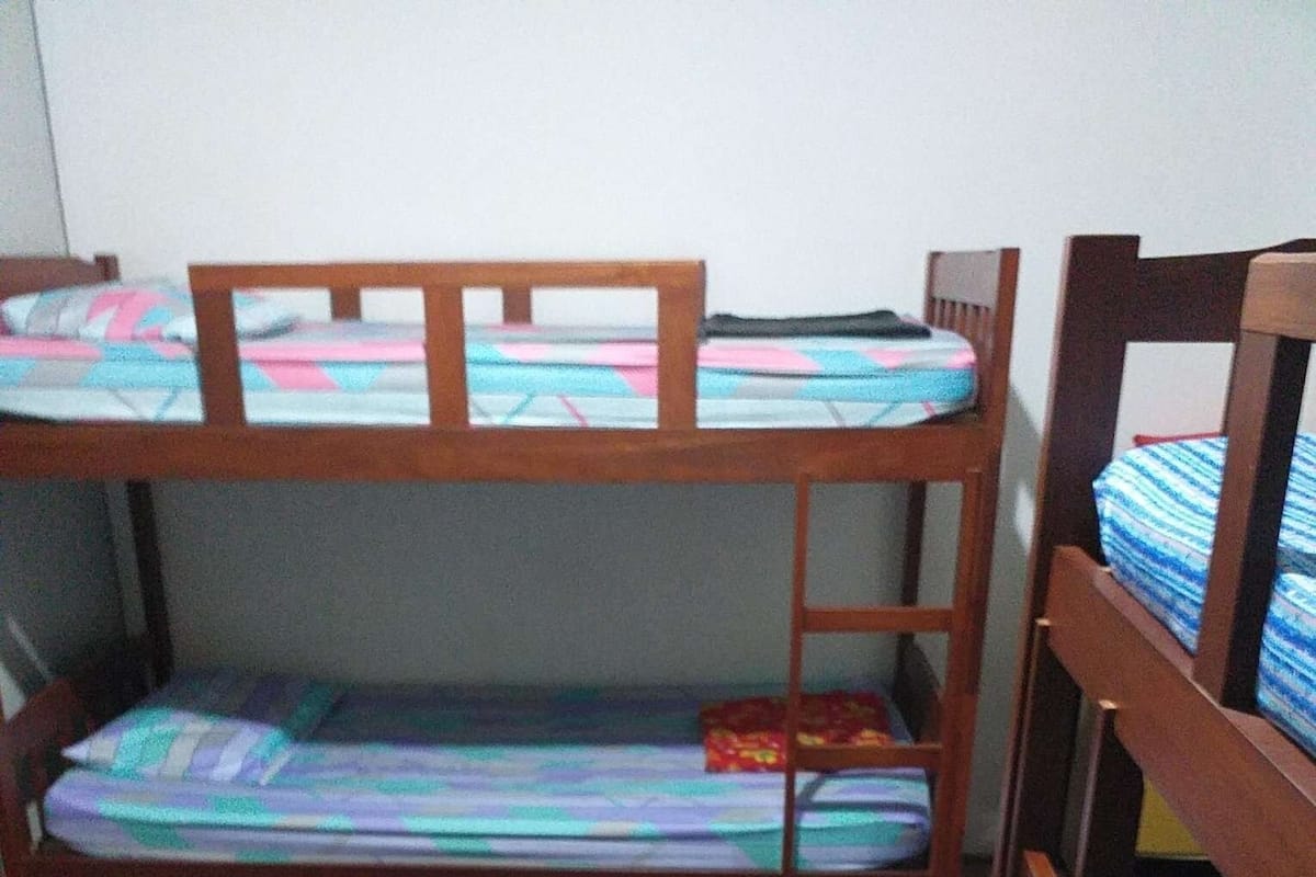 Habitación con literas, suelo de madera y una cama con colcha estampada.