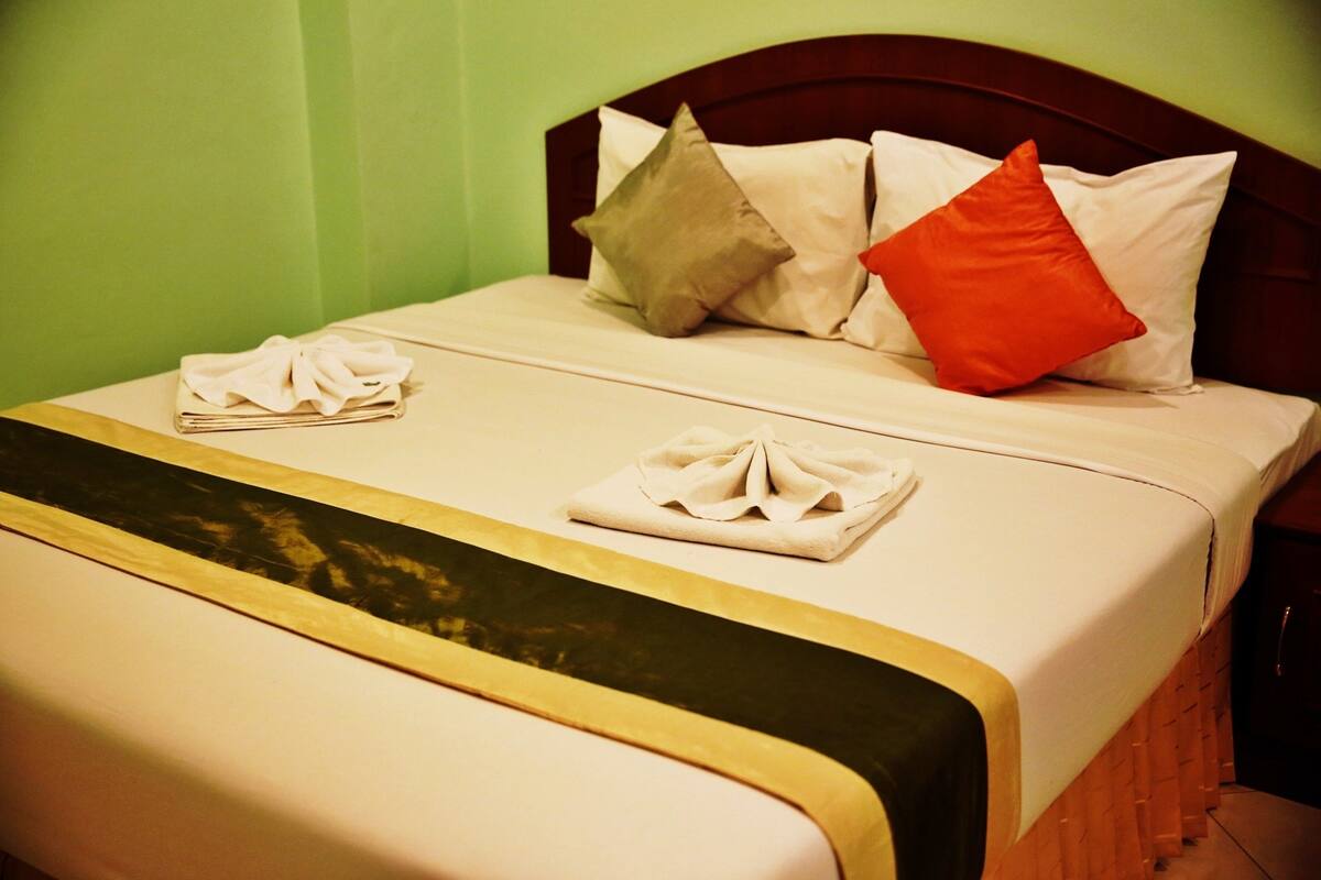 A neatly made bed with a wooden headboard, a beige bedspread, and two pillows in different colors.