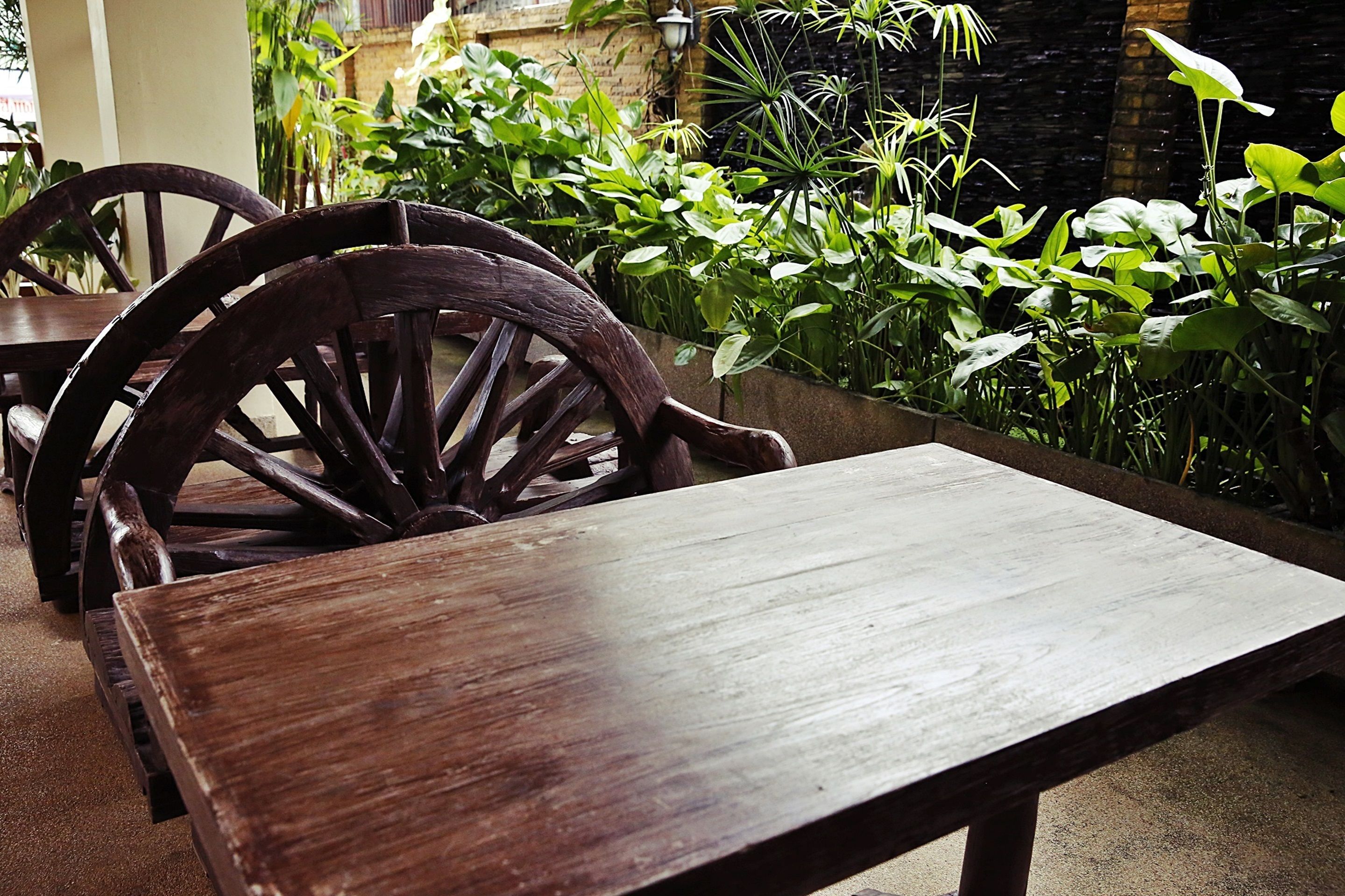 A wooden table and chairs in an outdoor setting with lush greenery.
