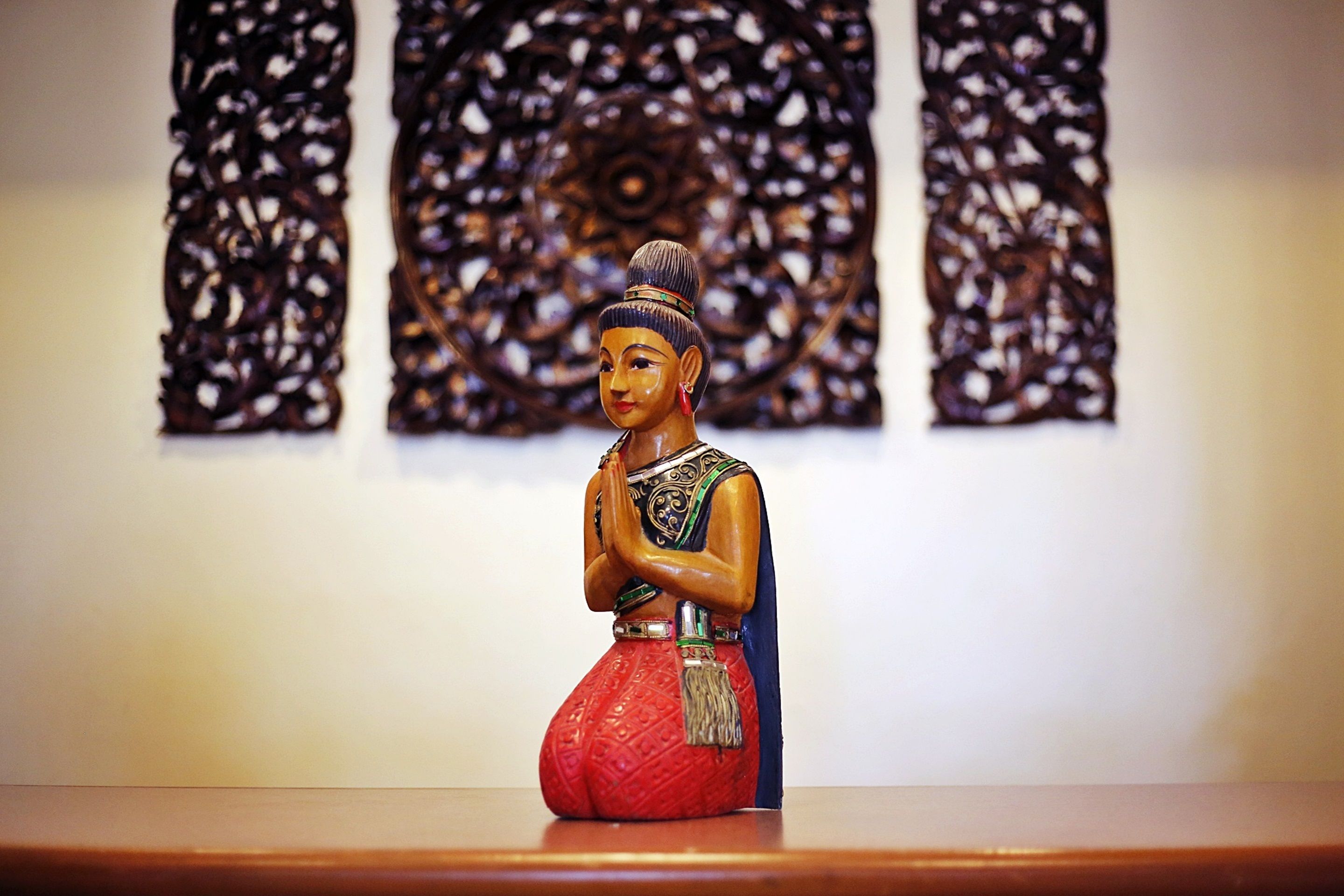 Estátua de uma figura vestida com traje tradicional, com padrões elaborados na parede ao fundo.