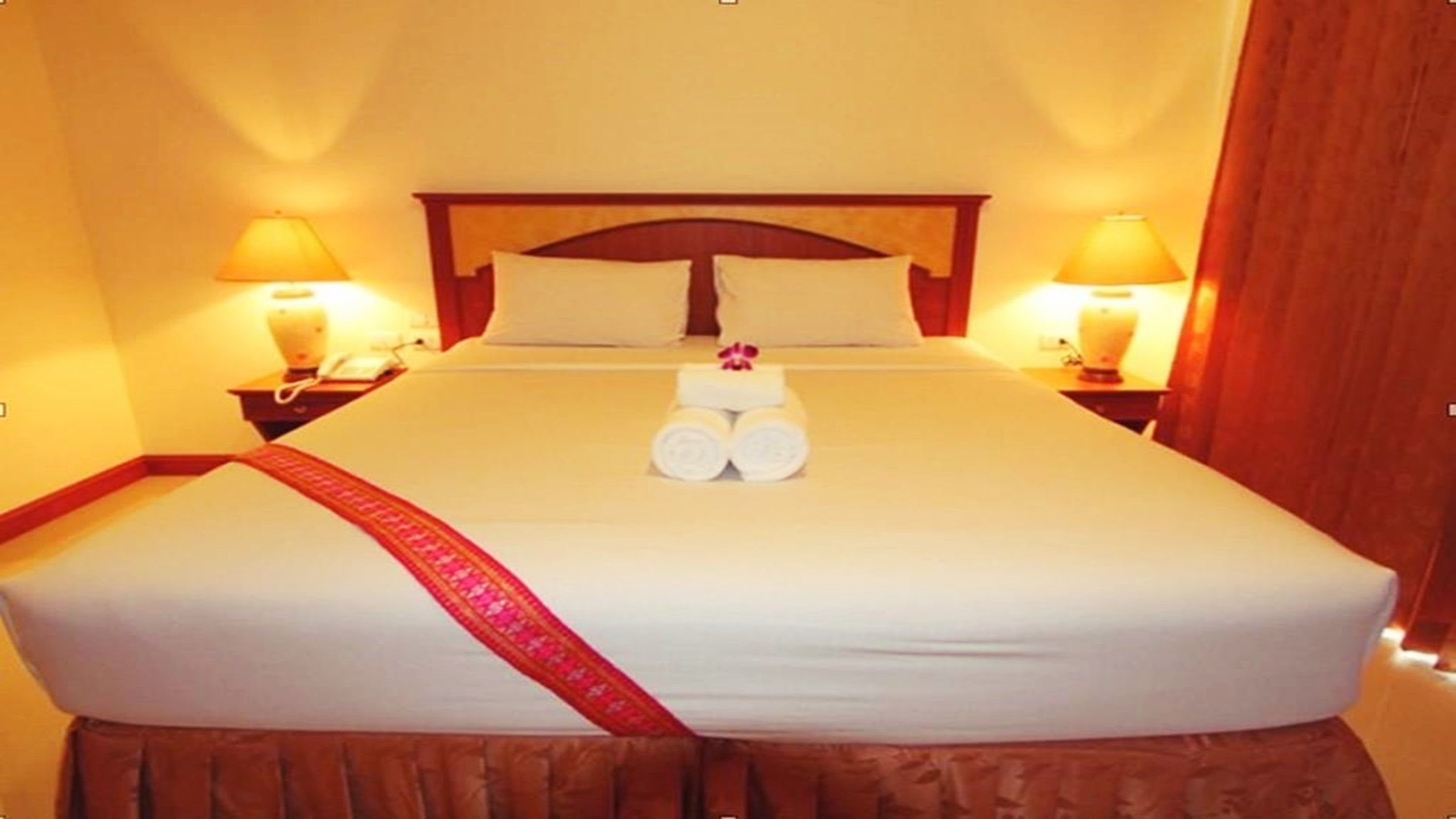 Ein Hotelzimmer mit einem großen Bett, zwei Nachttischlampen und einem roten dekorativen Zierstreifen auf der Bettdecke.