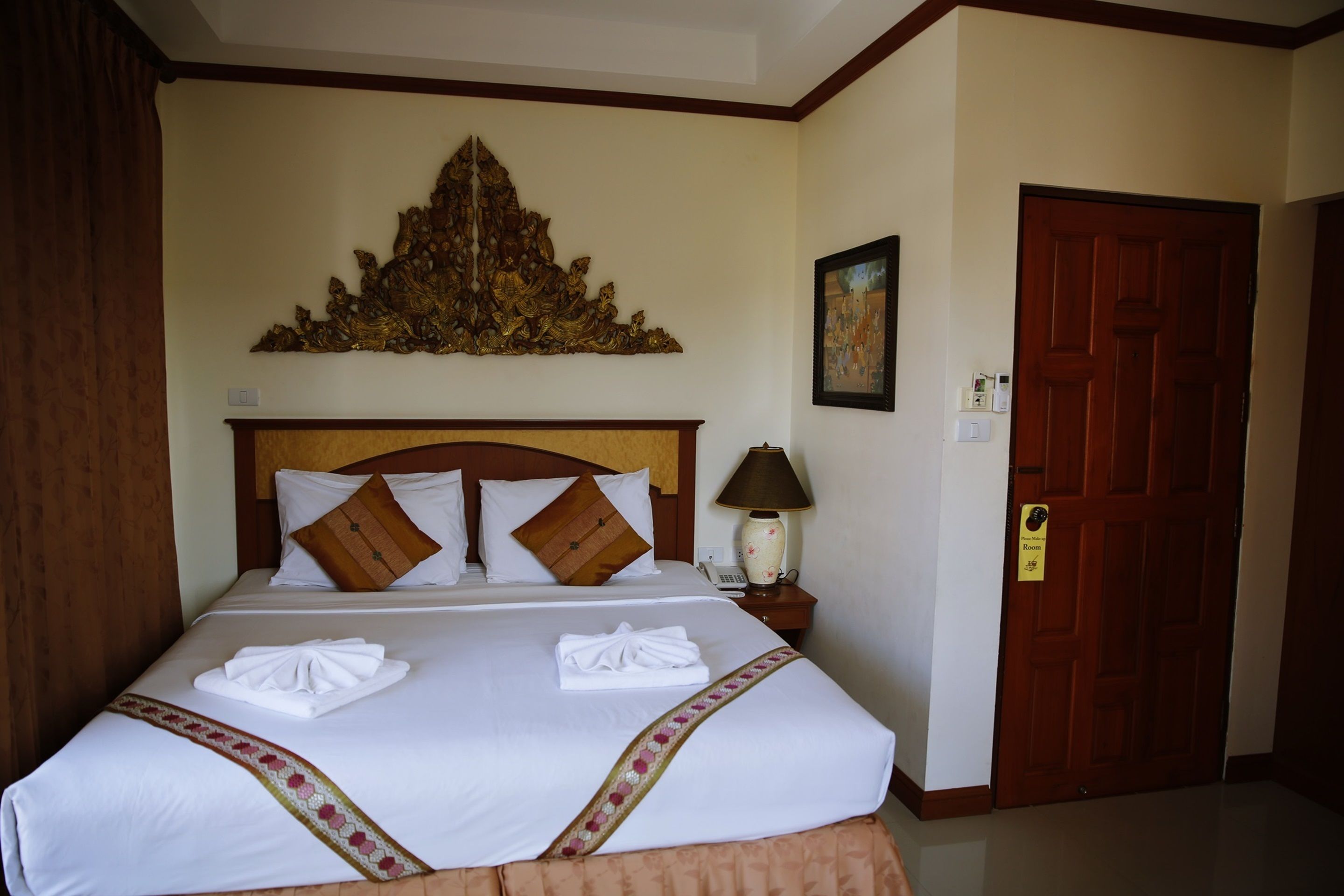 Une chambre d’hôtel avec un grand lit, une tête de lit en bois, un élément décoratif mural, une table de chevet avec une lampe et une porte avec une pancarte.