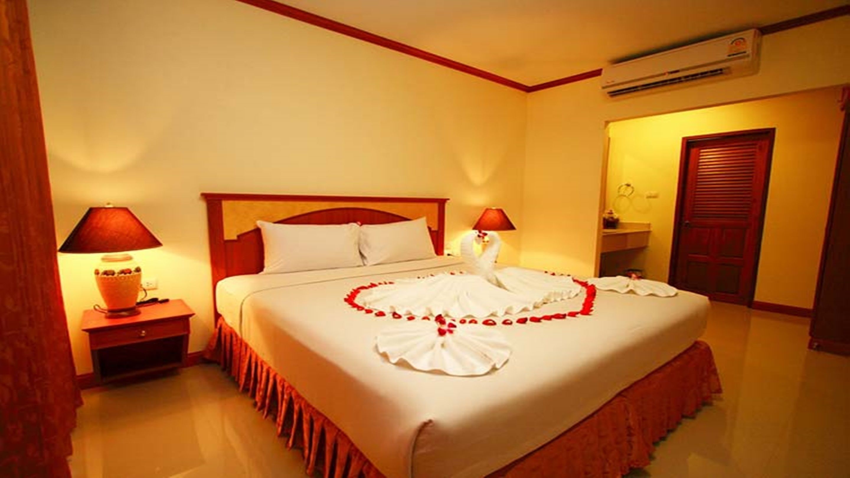 Habitación de hotel con una cama grande, dos lámparas de noche, un cabecero de madera y un cisne decorativo hecho de tela blanca sobre la cama.