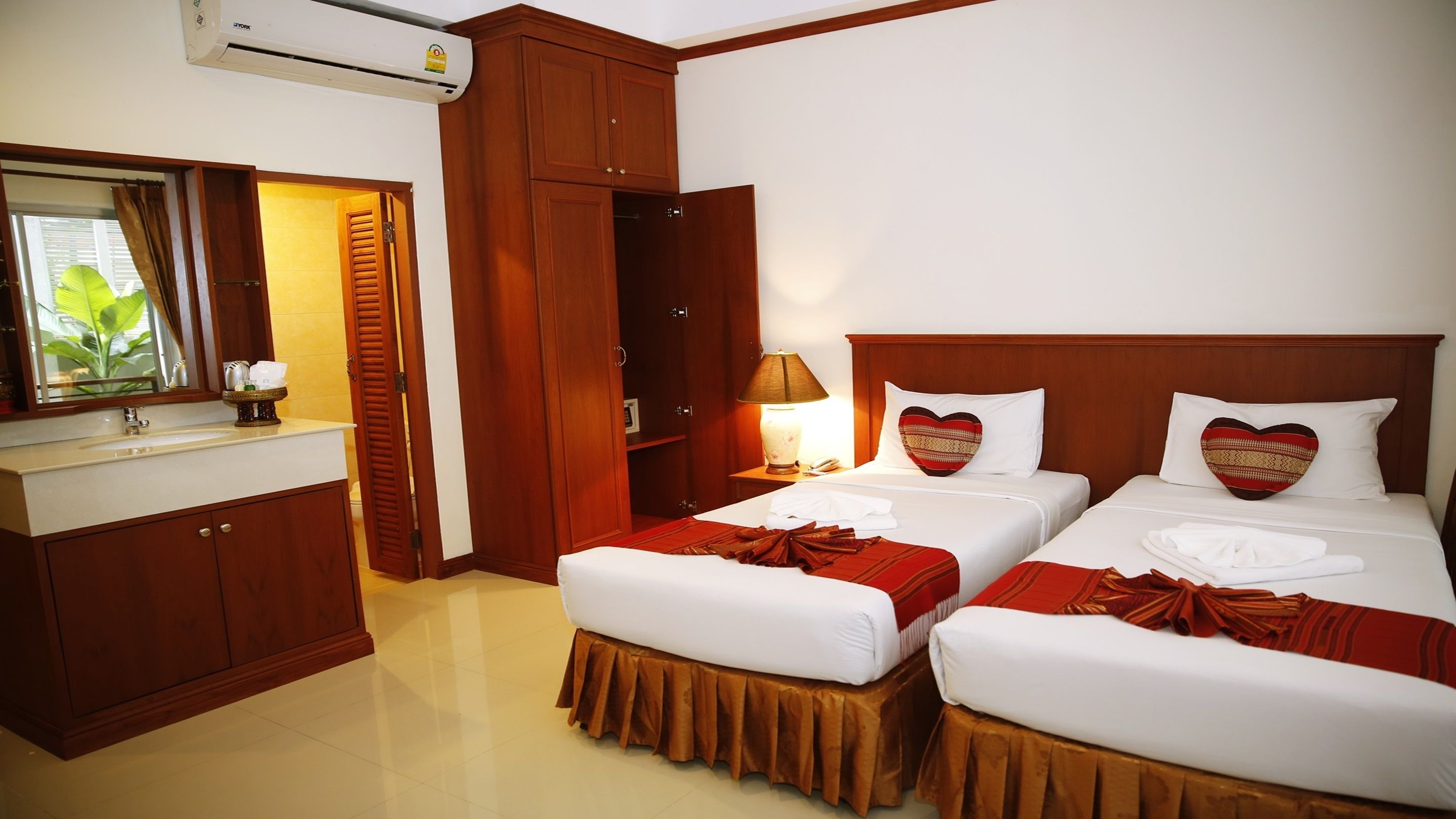 A hotel room with two beds, a vanity with a mirror, and a wooden wardrobe.