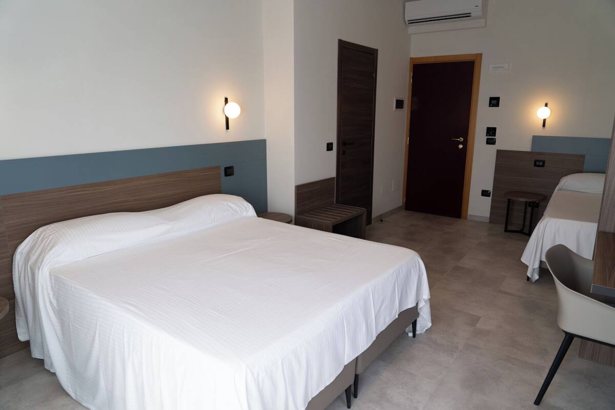 A hotel room with a large bed, a desk, a chair, and a bench.