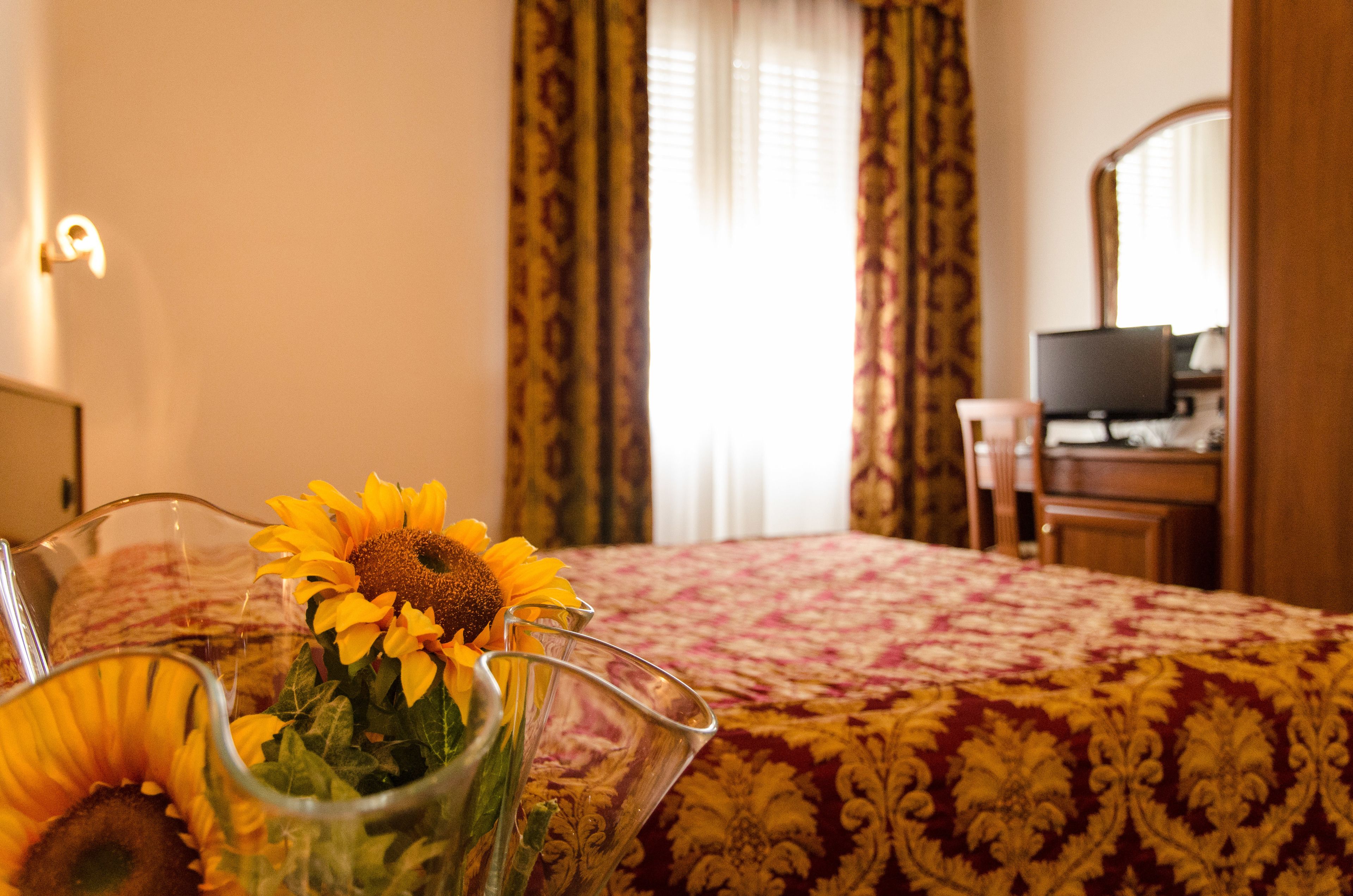 Une chambre d’hôtel avec un lit, une télévision, un bureau et un vase rempli de tournesols.