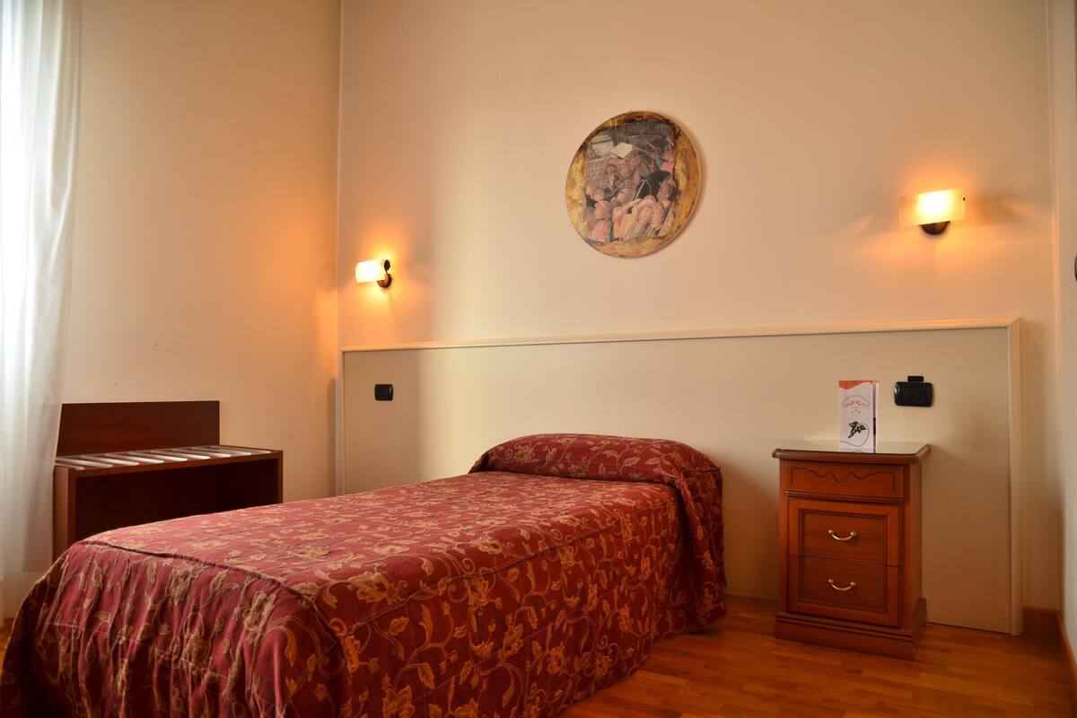 A bedroom with a bed, bedside table, and a wall-mounted lamp.
