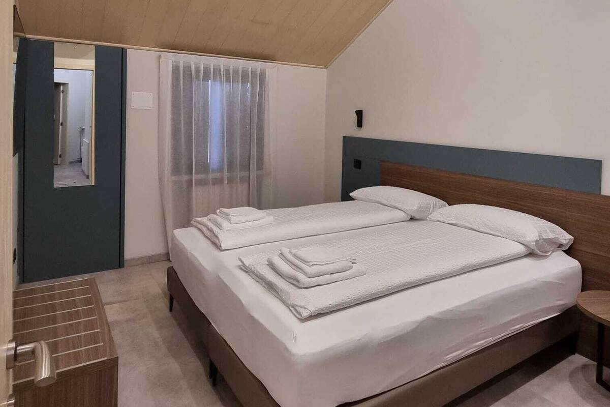 A modern bedroom with a large bed, a wooden ceiling, a mirror, and a bedside table.