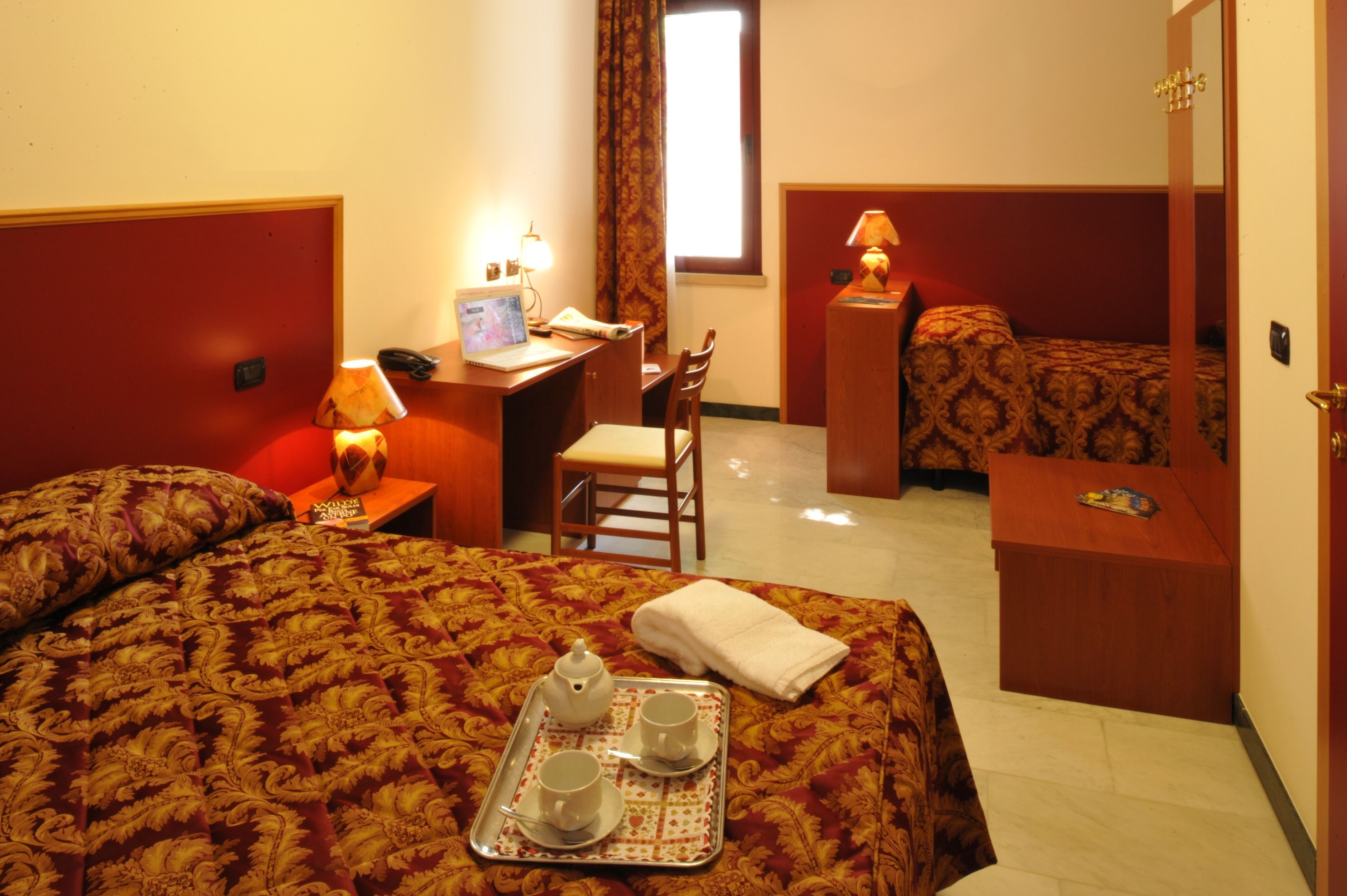 Habitación de hotel con cama, escritorio, silla, mesita y bandeja con tazas y tetera.