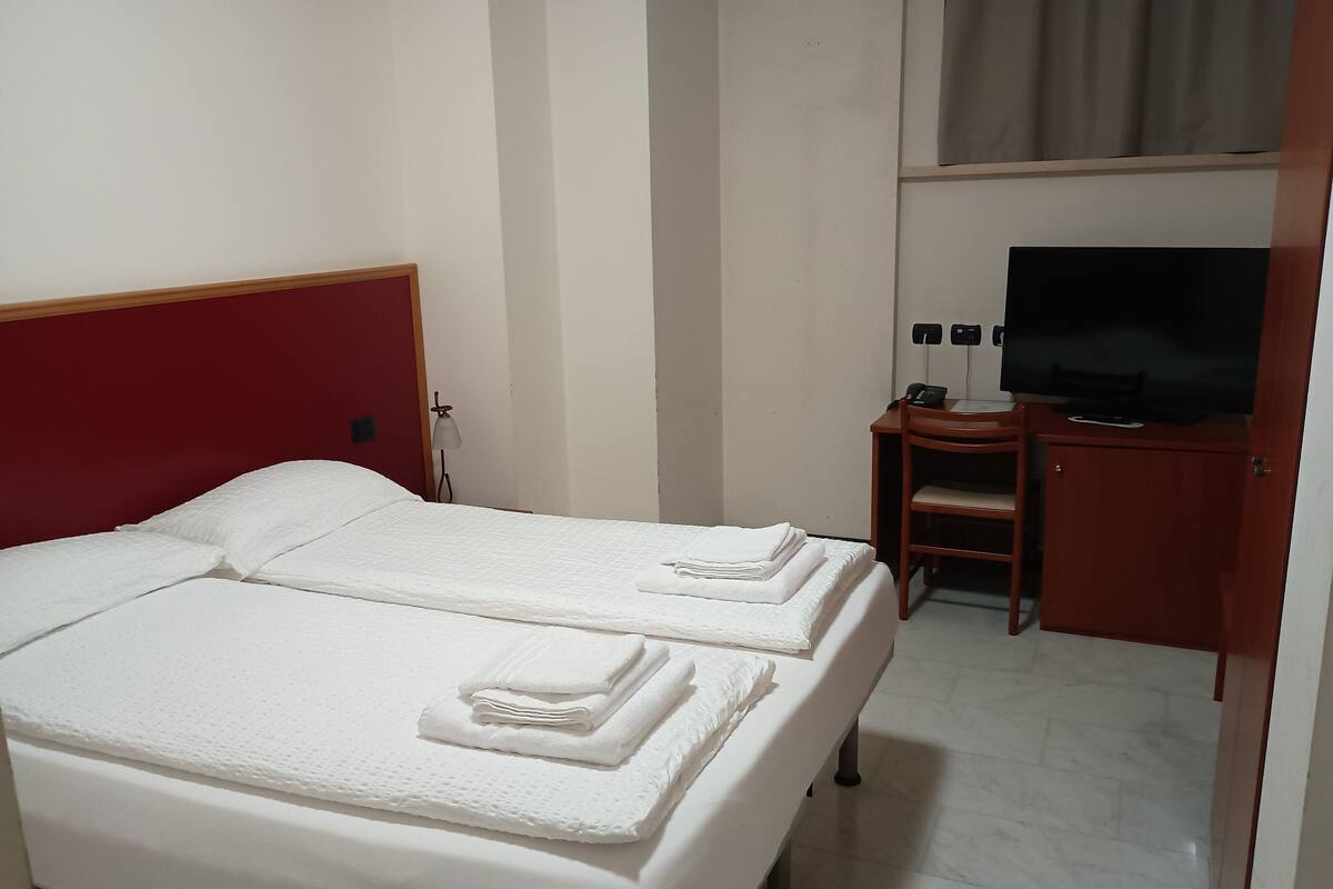 A hotel room with two beds, a desk, a chair, a television, and a wardrobe.