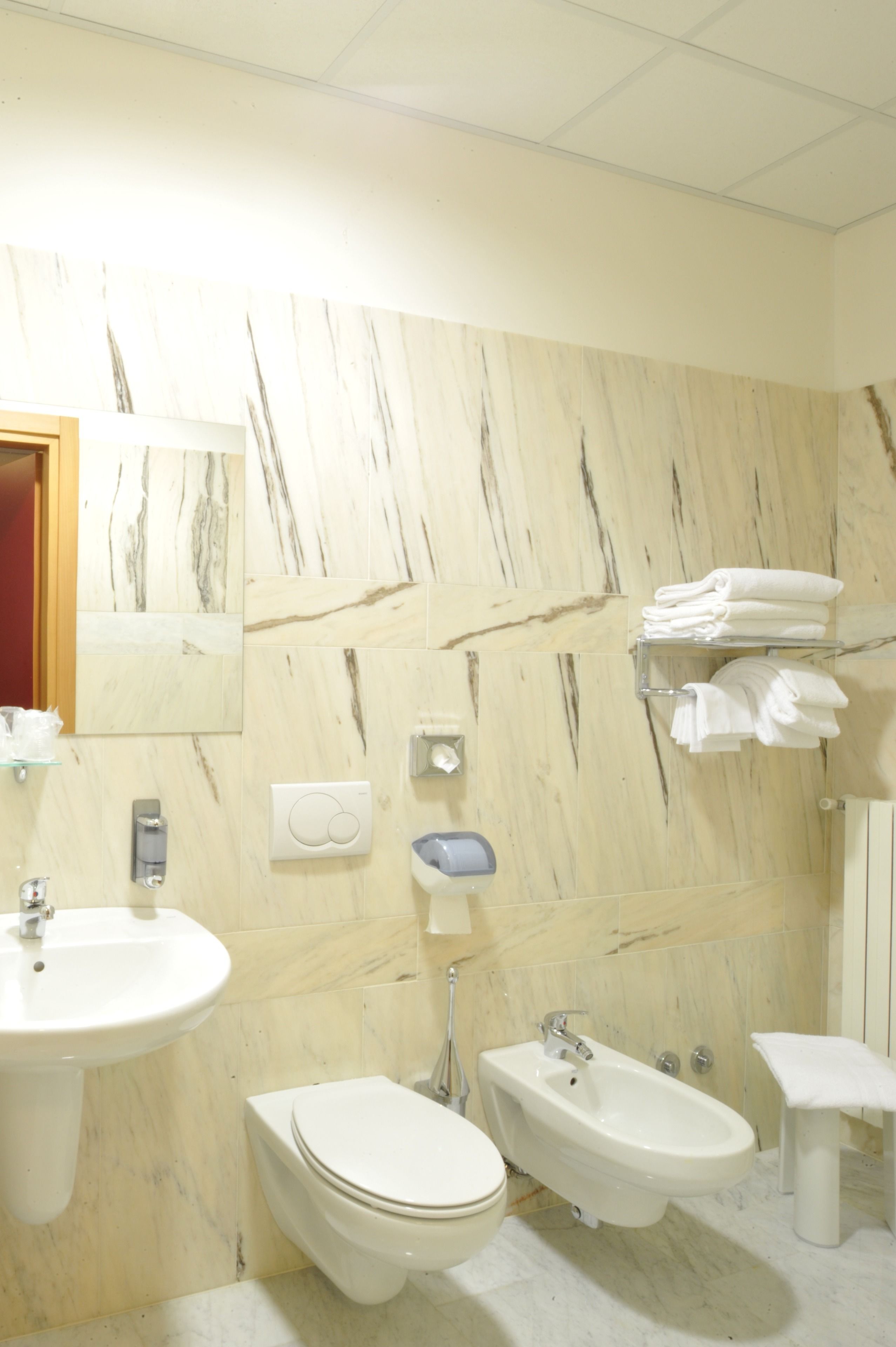 Un baño con pared de mármol, lavamanos, inodoro, bidé y un perchero para toallas.