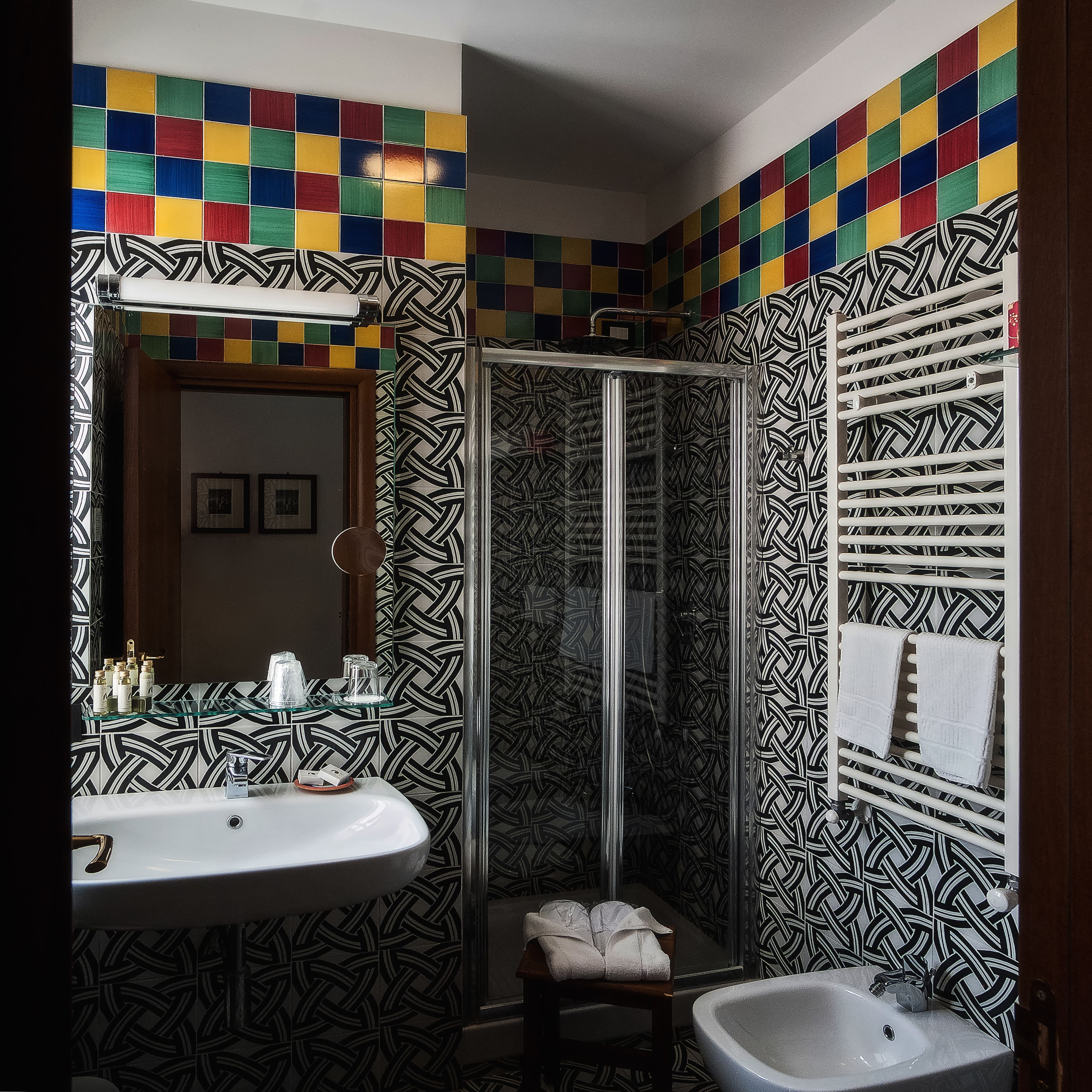 Un baño con lavamanos blanco, cabina de ducha de vidrio y paredes con diseño.