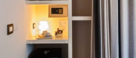 A compact hotel room with a bed, a wardrobe, a small desk with a lamp, and a mini-fridge.