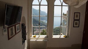 Habitación con dos grandes ventanales arqueados que ofrecen vistas a un paisaje montañoso y una masa de agua.