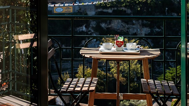 Un balcón con mesa y sillas, con vistas a un pueblo en la ladera con edificios y vegetación.