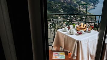 Een balkon met een ontbijttafel, met uitzicht op een kustlandschap.
