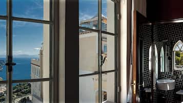 A room with a large window overlooking a coastal cityscape, a bathroom with a sink and mirror, and a patterned wall.