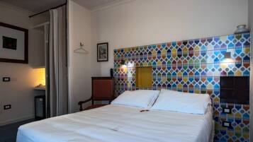 Habitación de hotel con cama, una silla, una mesita y una pared de azulejos coloridos.