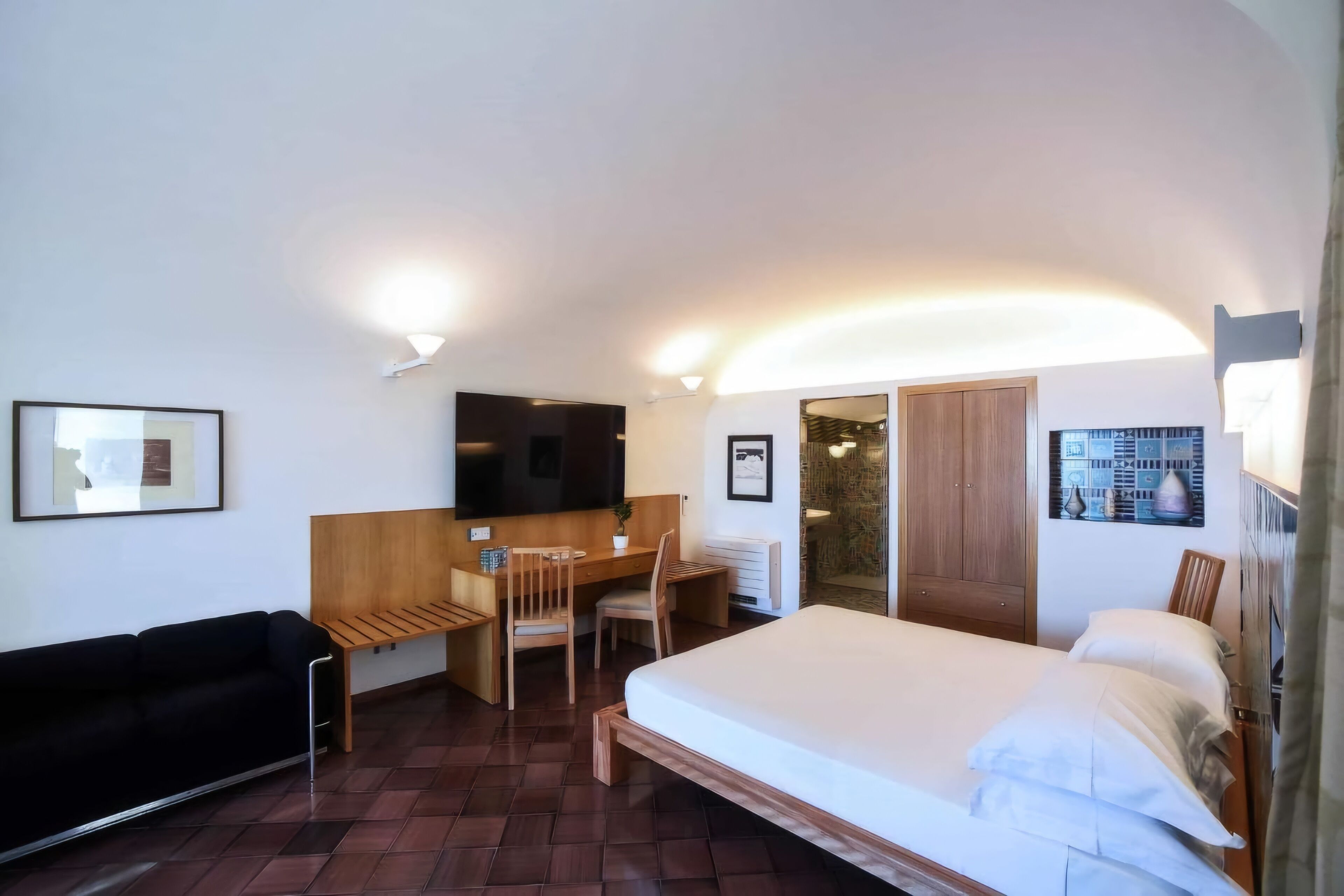 A compact hotel room with a bed, a desk, a chair, a sofa, and a television.
