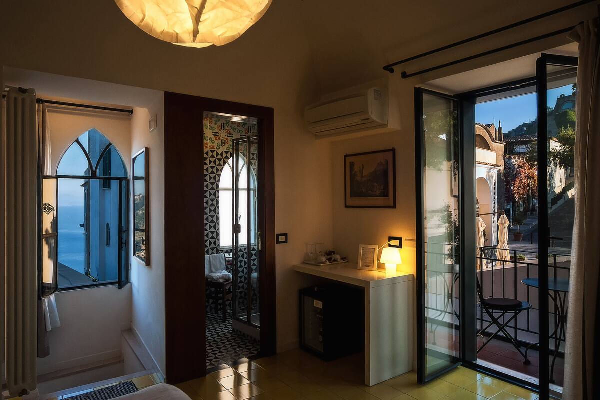 Une chambre d’hôtel avec vue sur la mer, un bureau avec une lampe et un balcon avec des sièges d’extérieur.