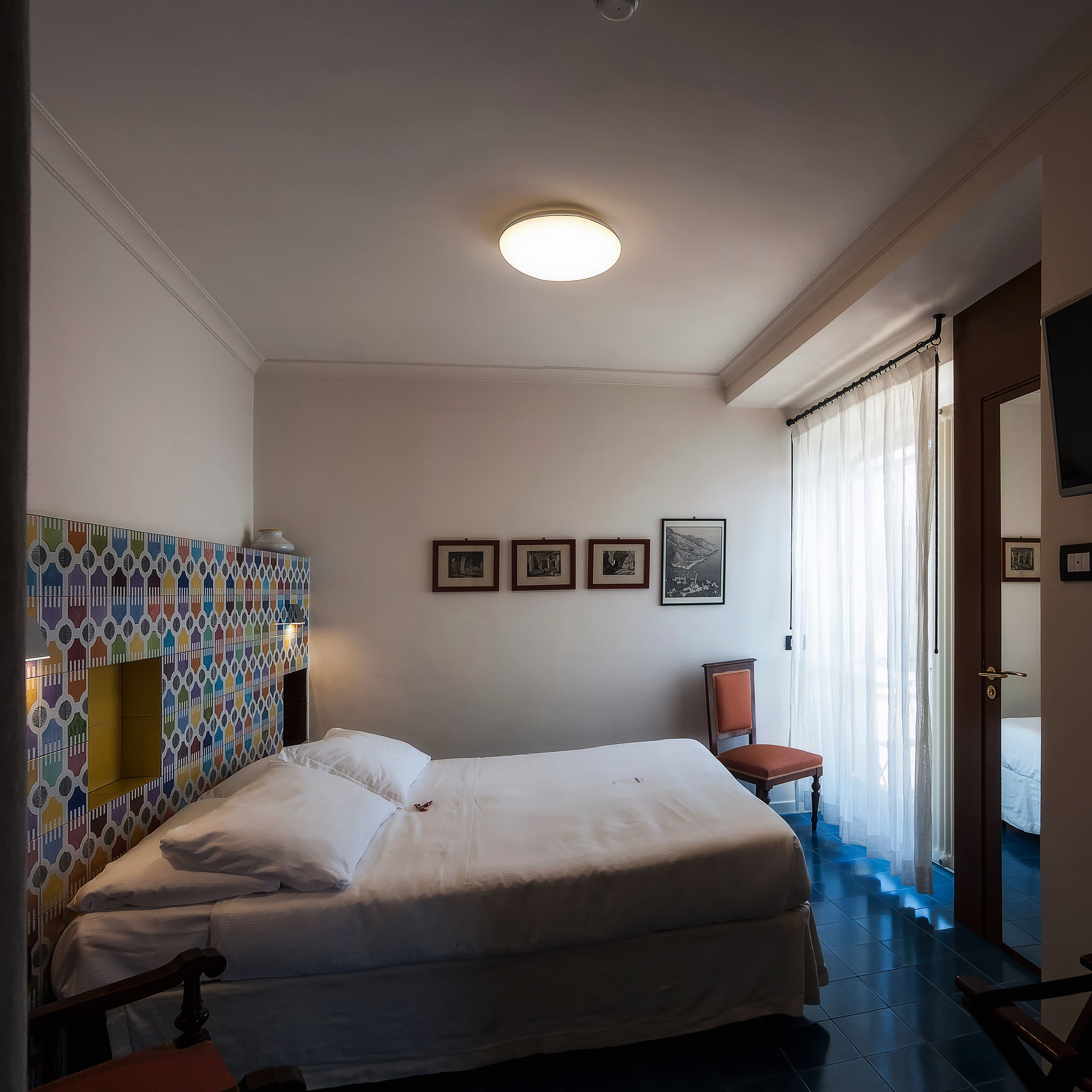 A hotel room with a bed, a chair, a TV, and a window with curtains.
