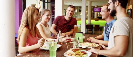 A group of people dining at a wooden table with various dishes and drinks.