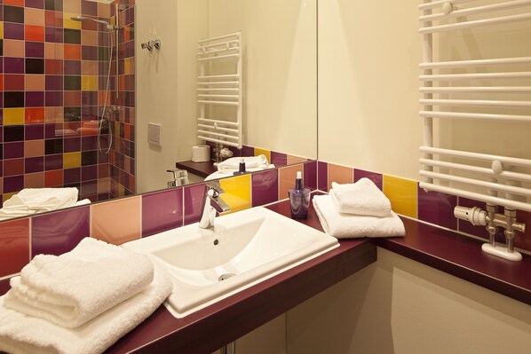 A bathroom with a tiled shower, a sink with a mirror, and a towel rack.