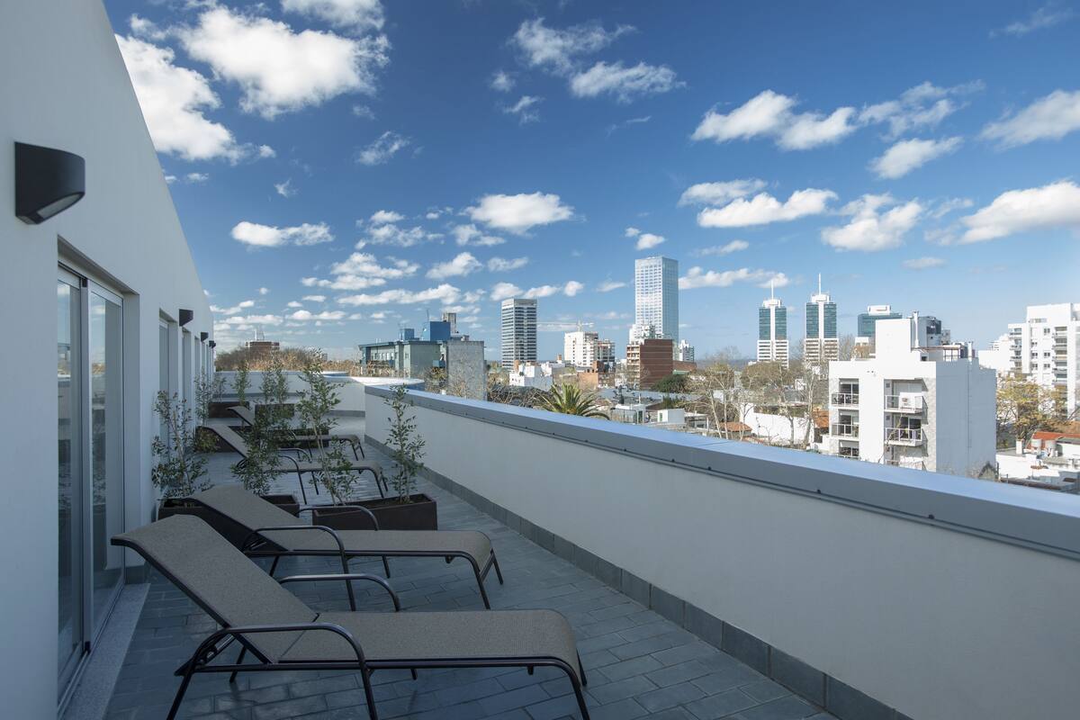 Una terraza en la azotea con sillones de descanso, vistas al horizonte de la ciudad y cielo despejado.