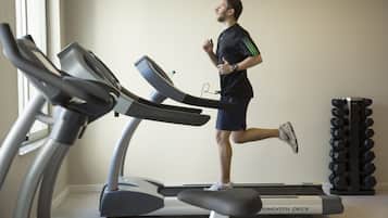 A person running on a treadmill in a gym with a dumbbell rack in the background.
