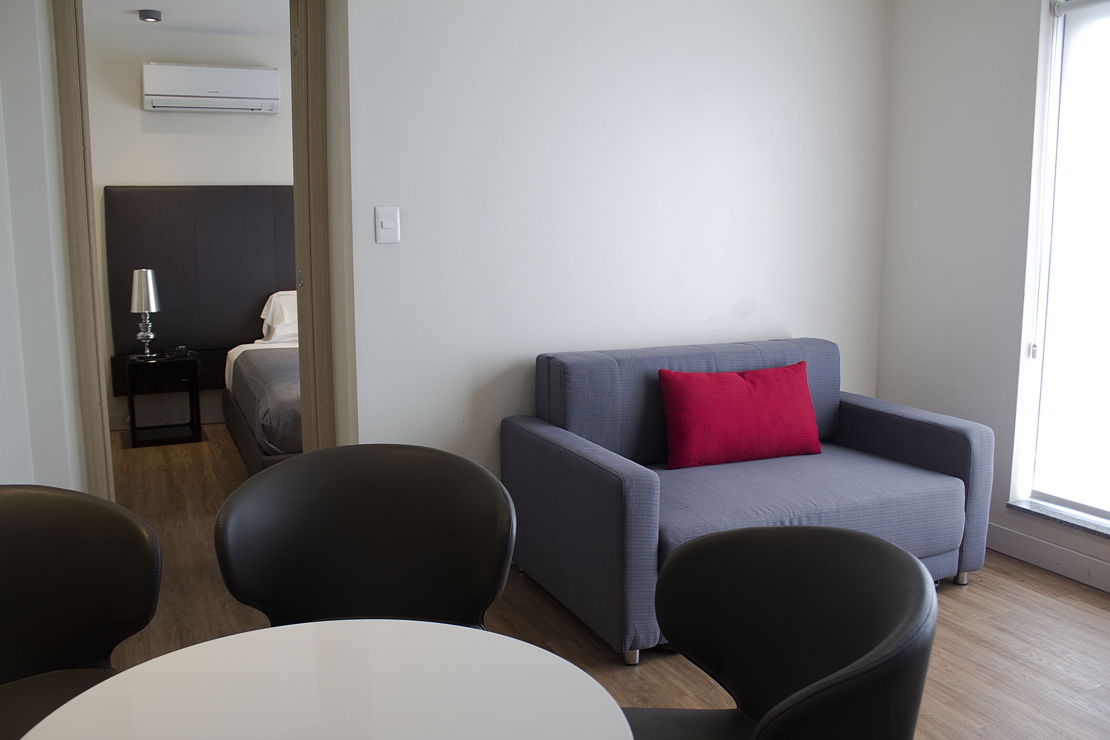 Une pièce moderne avec un canapé gris, un coussin rouge et une table blanche avec des chaises noires.