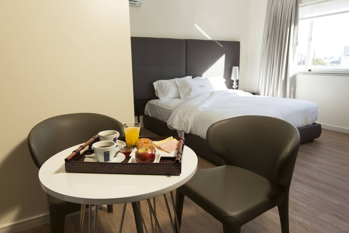 Una habitación de hotel con cama, una mesita de noche con desayuno, y una silla.