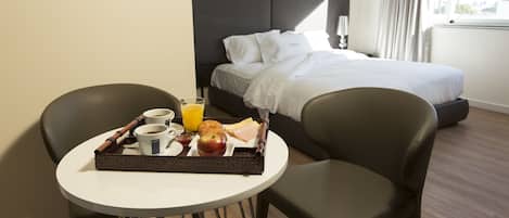 Una habitación de hotel con cama, una mesita de noche con desayuno, y una silla.