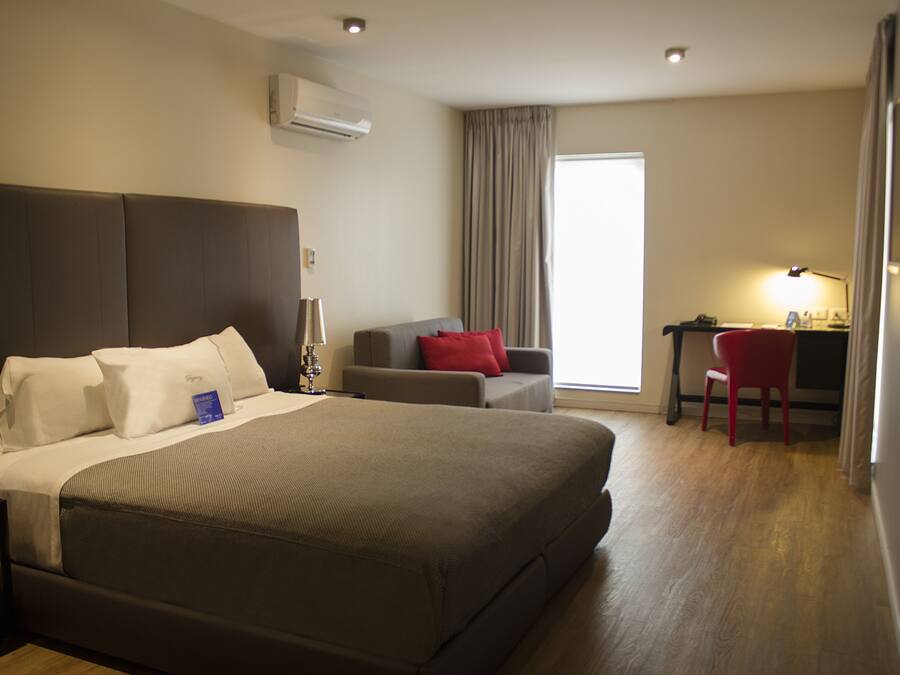 Una habitación de hotel con una cama grande, un escritorio, una silla y un ventanal con cortinas.